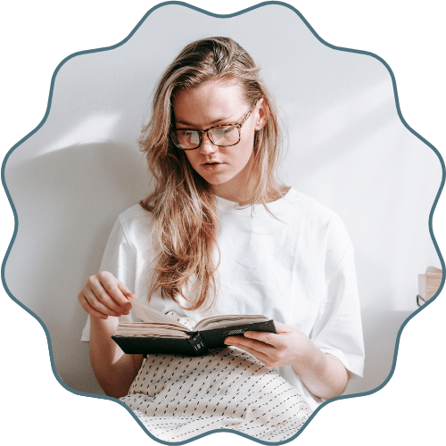 A young person sitting in a cozy chair, reading a hardcover book.